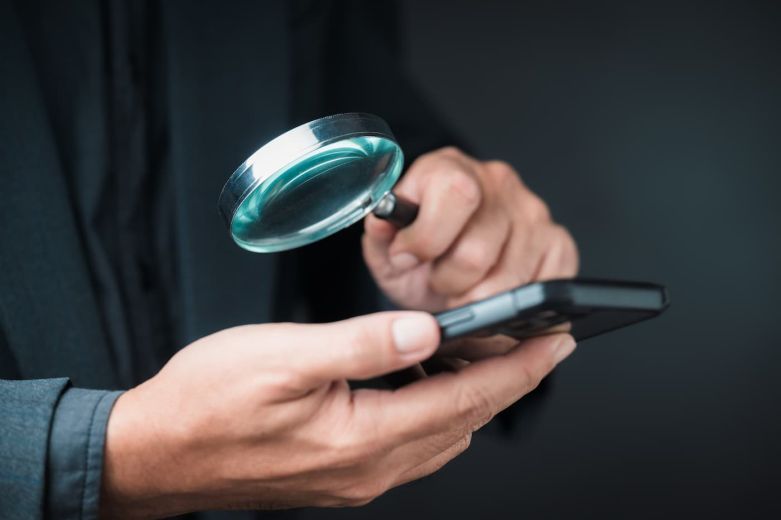Eine Lupe über einem Smartphone als Symbolbild für die KI Konsum Studie