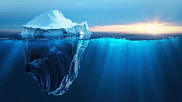 **Alternativtext:** Illustration eines Eisbergs im Meer: Über der Wasseroberfläche ist nur die kleine, schneebedeckte Spitze zu sehen, während der weitaus größere Teil des Eisbergs unter Wasser verborgen liegt. Das Bild symbolisiert unsichtbare Reformen, deren Wirkung erst unter der Oberfläche erkennbar wird.